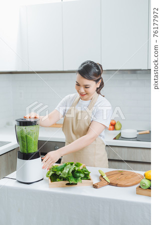 Vegetable smoothie woman blending green smoothies with blender home in kitchen Vegetable smoothie woman blending green smoothies with blender home in kitchen 76177972