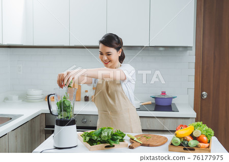 Vegetable smoothie woman blending green smoothies with blender home in kitchen Vegetable smoothie woman blending green smoothies with blender home in kitchen 76177975
