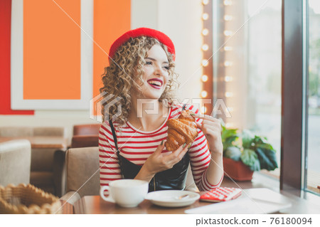 Cute young woman in red beret having a french breakfast Cute young woman in red beret having a french breakfast 76180094