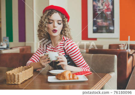 Cute woman in red beret drinking coffee in cafe Cute woman in red beret drinking coffee in cafe 76180096