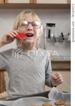 Happy boy tastes freshly baked cookies. Child in the kitchen prepares cookies. Happy boy tastes freshly baked cookies. Child in the kitchen prepares cookies. 76183072