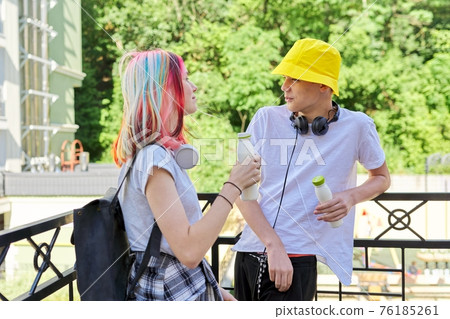 Couple of college students talking having rest drinking milk drink in bottle outdoors Couple of college students talking having rest drinking milk drink in bottle outdoors 76185261