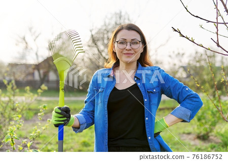 Spring gardening, portrait of mature smiling woman gardener with rake looking at camera 76186752