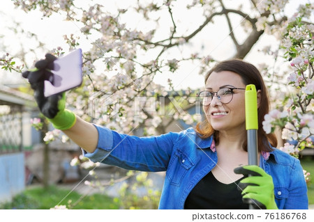 Happy woman in blooming garden taking selfie photo on smartphone Happy woman in blooming garden taking selfie photo on smartphone 76186768