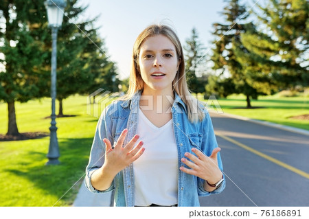Gesturing young beautiful woman talking at camera, teenager student giving interview Gesturing young beautiful woman talking at camera, teenager student giving interview 76186891