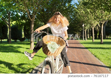 Happy young woman riding bike on road in park, beautiful hipter teenager having fun and laughing Happy young woman riding bike on road in park, beautiful hipter teenager having fun and laughing 76187117