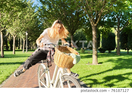 Happy young woman riding bike on road in park, beautiful hipter teenager having fun and laughing Happy young woman riding bike on road in park, beautiful hipter teenager having fun and laughing 76187127