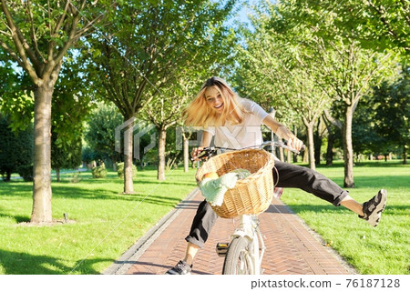 Happy young woman riding bike on road in park, beautiful hipter teenager having fun and laughing Happy young woman riding bike on road in park, beautiful hipter teenager having fun and laughing 76187128