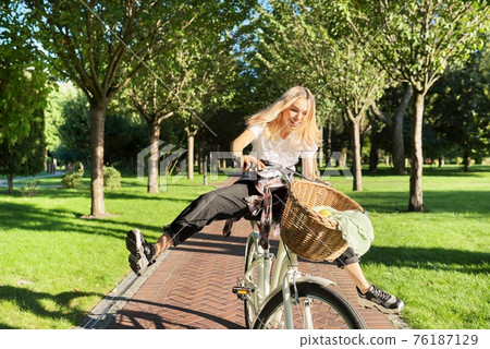 Happy young woman riding bike on road in park, beautiful hipter teenager having fun and laughing Happy young woman riding bike on road in park, beautiful hipter teenager having fun and laughing 76187129