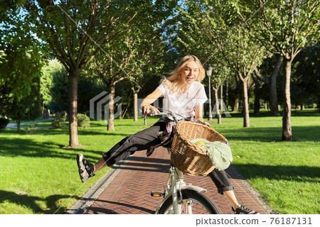 Happy young woman riding bike on road in park, beautiful hipter teenager having fun and laughing Happy young woman riding bike on road in park, beautiful hipter teenager having fun and laughing 76187131