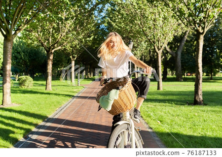 Happy young woman riding bike on road in park, beautiful hipter teenager having fun and laughing Happy young woman riding bike on road in park, beautiful hipter teenager having fun and laughing 76187133