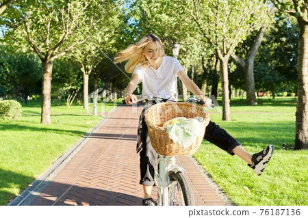 Happy young woman riding bike on road in park, beautiful hipter teenager having fun and laughing Happy young woman riding bike on road in park, beautiful hipter teenager having fun and laughing 76187136