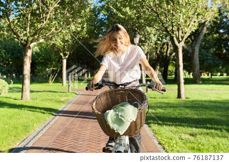 Young beautiful woman on vintage bike with basket rides on nature Young beautiful woman on vintage bike with basket rides on nature 76187137
