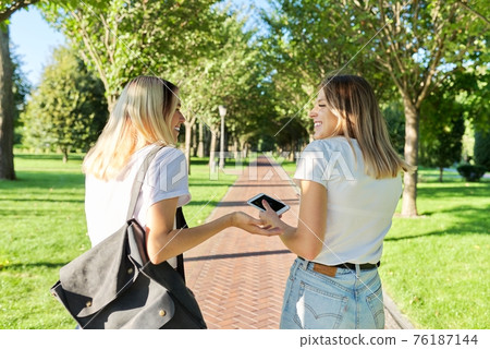 Two happy smiling talking girls teenagers students walking together, back view Two happy smiling talking girls teenagers students walking together, back view 76187144