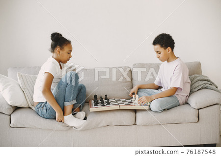 Boy and girl playing chess on the couch Boy and girl playing chess on the couch 76187548