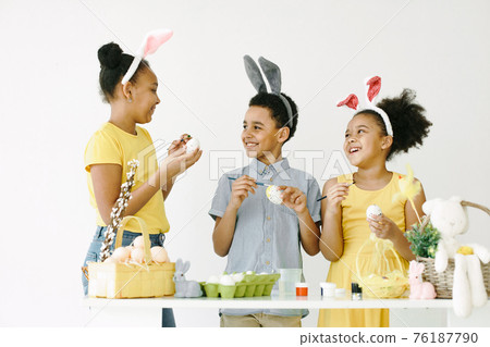 Children in yellow clothes paint Easter eggs 76187790