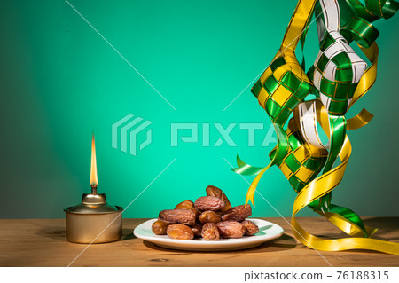 Muslim iftar of breaking of fast during Ramadan month with preserved sweet dates. Ketupat and pelita oil lamp as prop. 76188315