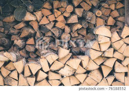Logs of firewood piled under the roof of slate. Fuel for stove heating. Country life. Wooden firewood stacked wall. Natural wood background. Firewood stacked in several rows Logs of firewood piled under the roof of slate. Fuel for stove heating. Country life. Wooden firewood stacked wall. Natural wood background. Firewood stacked in several rows 76188552