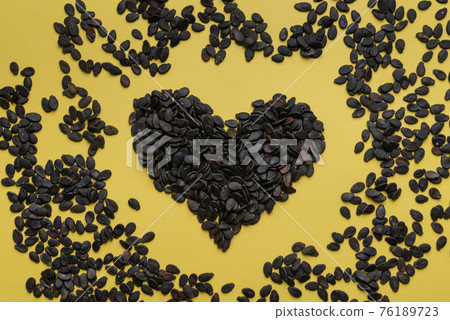 A pile of watermelon seeds on a yellow background in the shape of a heart 76189723