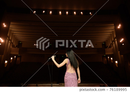 Beautiful singer against the auditorium. Back view girl in long gown performing on stage. Beautiful singer against the auditorium. Back view girl in long gown performing on stage. 76189995