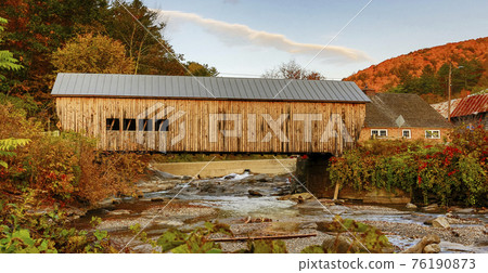 A historic yellow wooden covered bridge crosses a small stream in Autumn A historic yellow wooden covered bridge crosses a small stream in Autumn 76190873