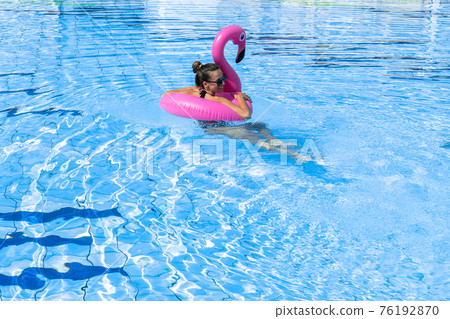 Young women pool. Happy young sexy girl in bikini swimsuit, sunglasses with pink inflatable flamingo float in blue water. Travel holidays vacation. Beauty, wellness, lifestyle. 76192870