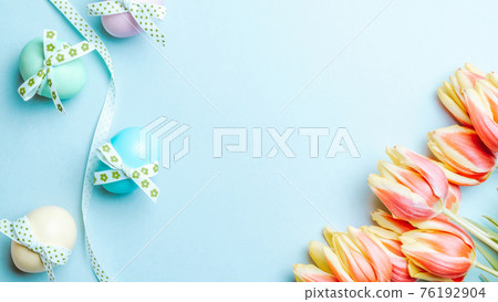 Easter eggs background. Colorful egg with tape ribbon, spring tulips, feathers on pastel blue background in Happy Easter decoration. Foil minimalist egg design, modern top view template. Easter eggs background. Colorful egg with tape ribbon, spring tulips, feathers on pastel blue background in Happy Easter decoration. Foil minimalist egg design, modern top view template. 76192904