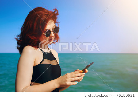 Red-haired woman writes message on her mobile phone. Red-haired woman writes message on her mobile phone. 76199631