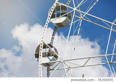 fragment of a ferris wheel against a blue sky with clouds, concept 76200895