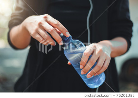 Female athlete opening the plastic cap of mineral water bottle Female athlete opening the plastic cap of mineral water bottle 76201385