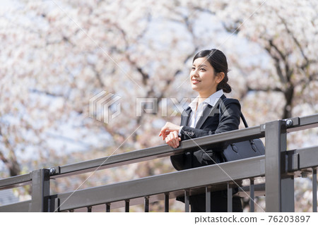 A business woman in a suit looking at a row of cherry blossom trees from the top of the bridge A business woman in a suit looking at a row of cherry blossom trees from the top of the bridge 76203897