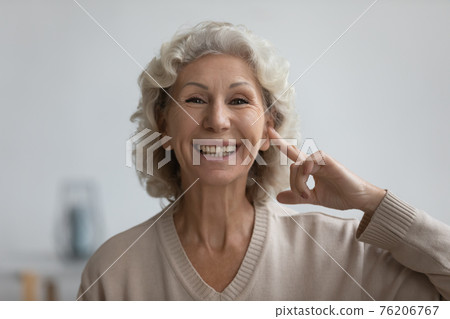 Portrait of happy senior woman pointing finger at her ear 76206767