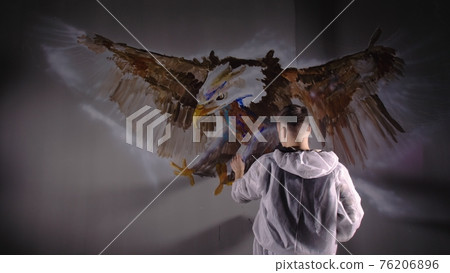 Artist designer draws an eagle on the wall. Craftsman decorator paints picture with acrylic oil color. Painter painter dressed in paint coat. Indoor. 76206896
