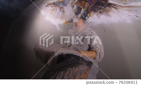 Artist designer draws an eagle on the wall. Craftsman decorator paints a picture with acrylic oil color. Vaper smokes vape. Dark magic cinematic look. 76206911