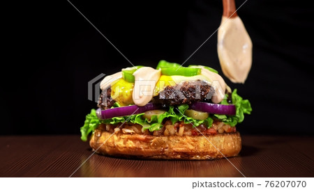 Craft burger is cooking on black background. Consist: sauce salsa, lettuce, red onion, pickle, cheese, chilli green pepper, bun, marbled meat beef. Craft burger is cooking on black background. Consist: sauce salsa, lettuce, red onion, pickle, cheese, chilli green pepper, bun, marbled meat beef. 76207070
