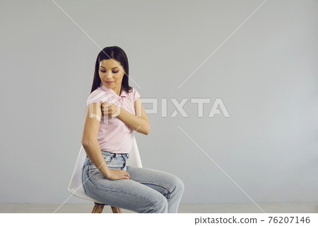 Happy young lady sitting on a chair shows her arm after receiving a Covid-19 shot Happy young lady sitting on a chair shows her arm after receiving a Covid-19 shot 76207146