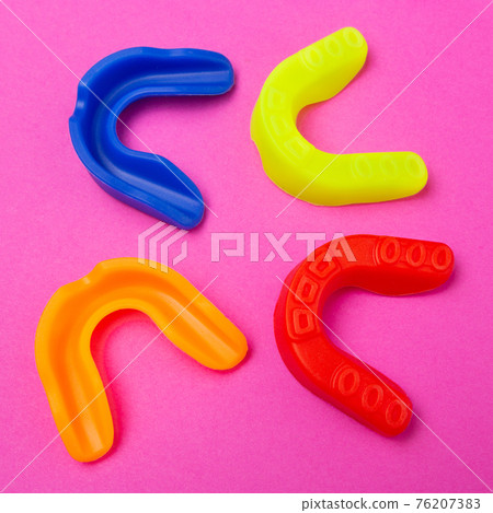 four multi-colored boxing mouthguards, lies on a pink background four multi-colored boxing mouthguards, lies on a pink background 76207383