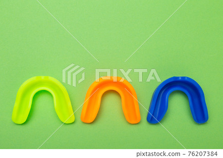 three colored boxing mouthguards, yellow green, blue and orange, lie on a green background, concept three colored boxing mouthguards, yellow green, blue and orange, lie on a green background, concept 76207384