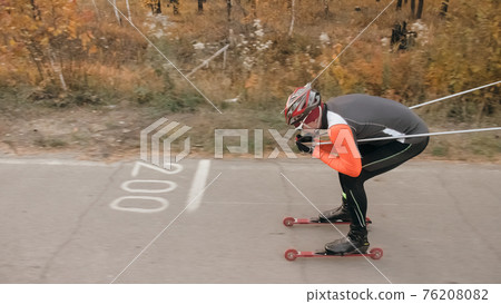Training an athlete on the roller skaters. Biathlon ride on the roller skis with ski poles, in the helmet. Autumn workout. Roller sport. Training an athlete on the roller skaters. Biathlon ride on the roller skis with ski poles, in the helmet. Autumn workout. Roller sport. 76208082