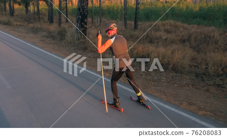 Training an athlete on the roller skaters. Biathlon ride on the roller skis with ski poles, in the helmet. Autumn workout. Roller sport. Training an athlete on the roller skaters. Biathlon ride on the roller skis with ski poles, in the helmet. Autumn workout. Roller sport. 76208083