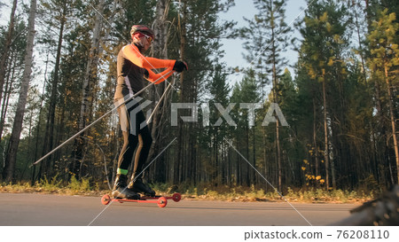 Training an athlete on the roller skaters. Biathlon ride on the roller skis with ski poles, in the helmet. Autumn workout. Roller sport. Training an athlete on the roller skaters. Biathlon ride on the roller skis with ski poles, in the helmet. Autumn workout. Roller sport. 76208110