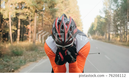 Training an athlete on the roller skaters. Biathlon ride on the roller skis with ski poles, in the helmet. Autumn workout. Roller sport. 76208112