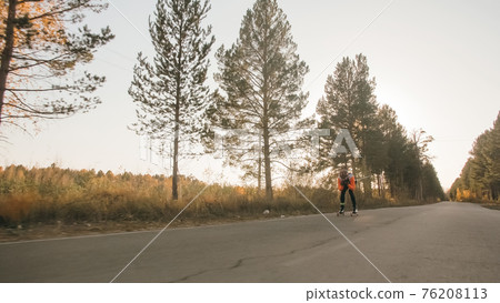 Training an athlete on the roller skaters. Biathlon ride on the roller skis with ski poles, in the helmet. Autumn workout. Roller sport. Training an athlete on the roller skaters. Biathlon ride on the roller skis with ski poles, in the helmet. Autumn workout. Roller sport. 76208113