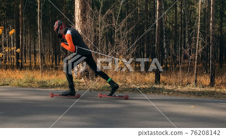 Training an athlete on the roller skaters. Biathlon ride on the roller skis with ski poles, in the helmet. Autumn workout. Roller sport. Athlete is getting ready to start. Training an athlete on the roller skaters. Biathlon ride on the roller skis with ski poles, in the helmet. Autumn workout. Roller sport. Athlete is getting ready to start. 76208142