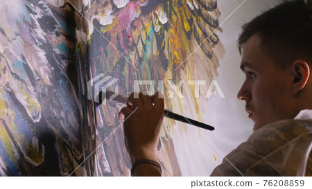 Artist designer draws an eagle on the wall. Craftsman decorator paints picture with acrylic oil color. Painter painter dressed in paint coat. Indoor. 76208859