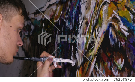 Artist designer draws an eagle on the wall. Craftsman decorator paints picture with acrylic oil color. Painter painter dressed in paint coat. Indoor. Artist designer draws an eagle on the wall. Craftsman decorator paints picture with acrylic oil color. Painter painter dressed in paint coat. Indoor. 76208870