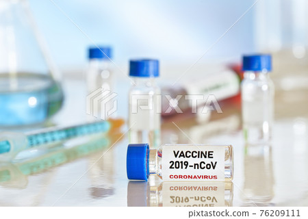 Coronavirus Covid 19 vaccine concept small glass vials with blue caps on white table, green orange syringe near closeup detail Coronavirus Covid 19 vaccine concept small glass vials with blue caps on white table, green orange syringe near closeup detail 76209111