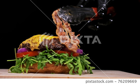 Craft burger is cooking on black background. Consist: sauce, arugula, tomato, onion, bacon, currant sauce, ricotta cheese, air bun and marble meat. 76209669