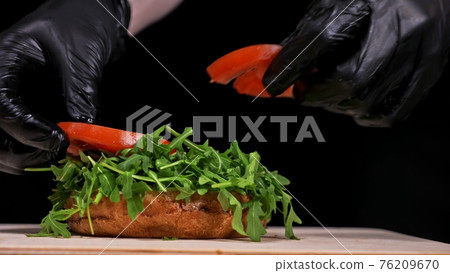 Craft burger is cooking on black background. Consist: sauce, arugula, tomato, onion, bacon, currant sauce, ricotta cheese, air bun and marble meat. 76209670