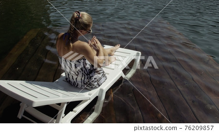 Woman lie on a sunbed in sunglasses and a boho silk shawl. Girl rest on a flood wood underwater pier. The pavement is covered with water in the lake. Woman lie on a sunbed in sunglasses and a boho silk shawl. Girl rest on a flood wood underwater pier. The pavement is covered with water in the lake. 76209857